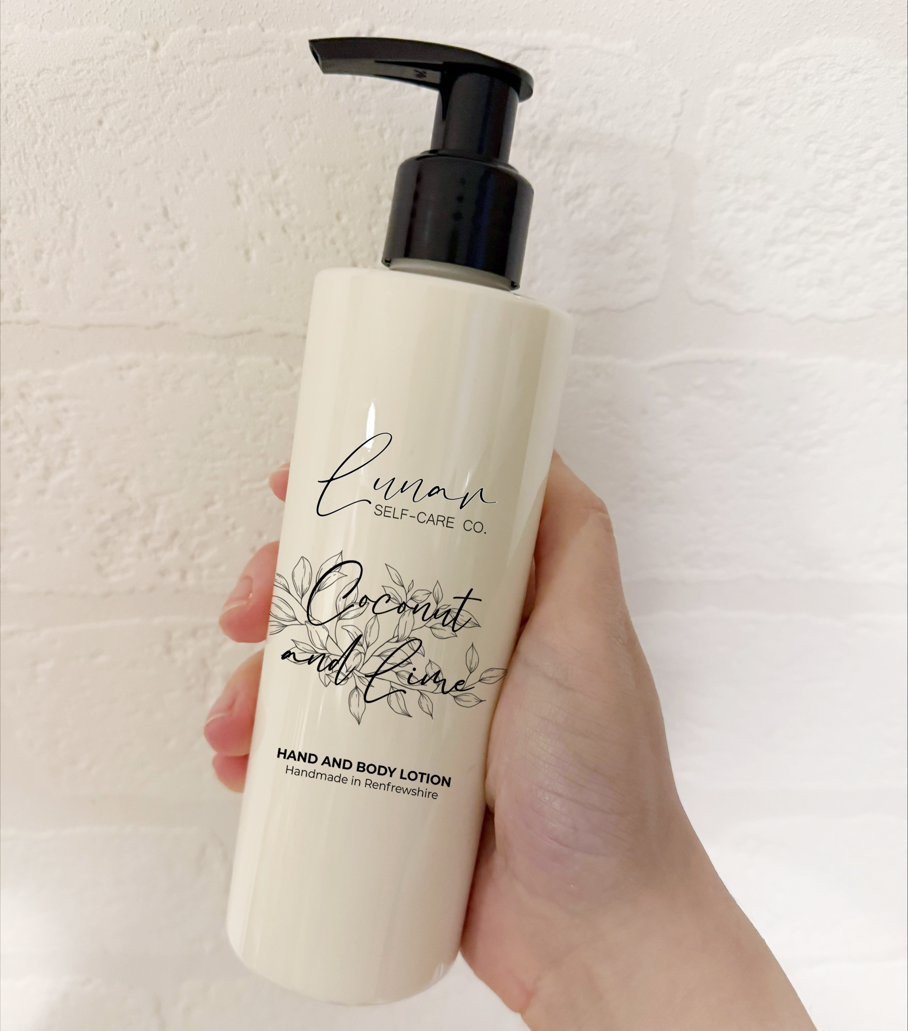 Hand holding a bottle of 'Coconut and Lime' hand and body lotion with a pump on a light background.