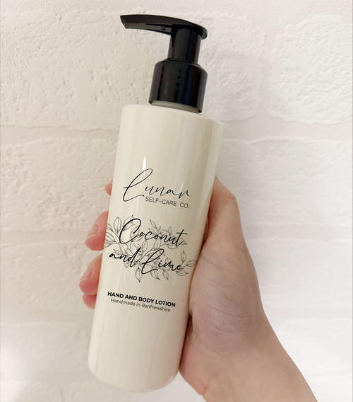Hand holding a bottle of 'Coconut and Lime' hand and body lotion with a pump on a light background.