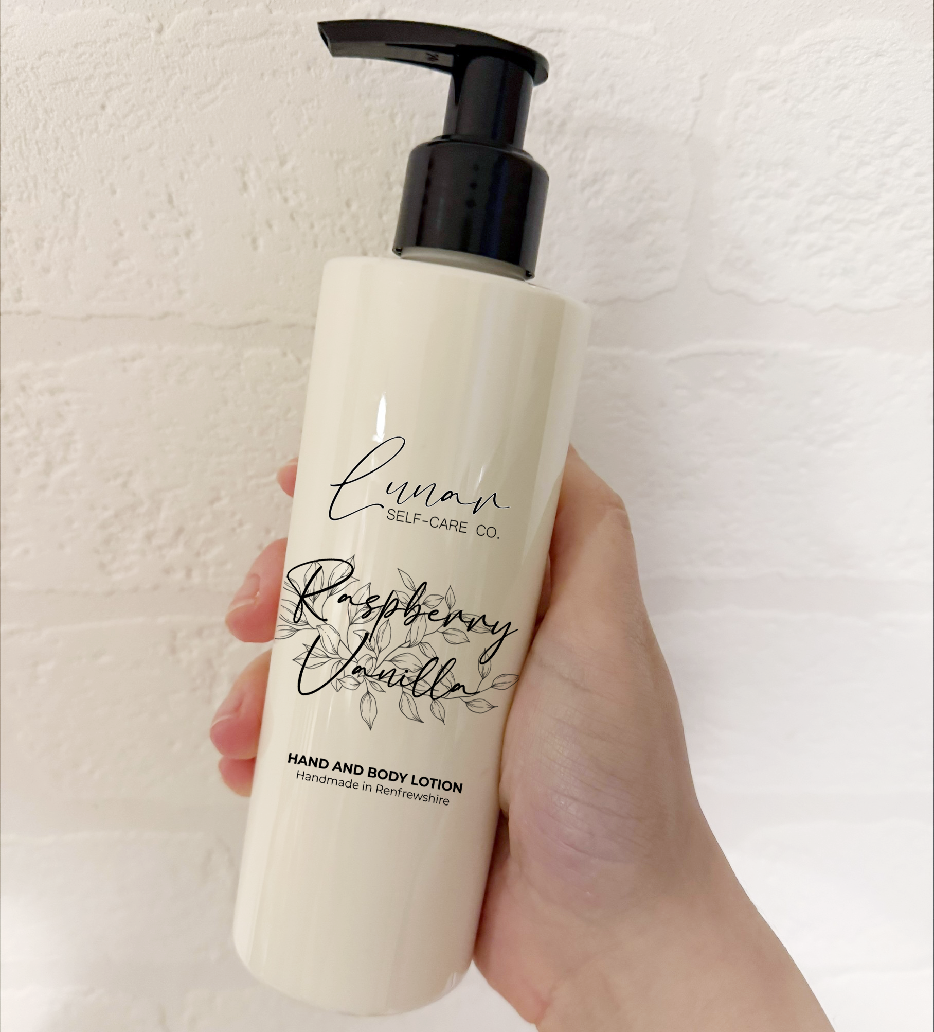 Hand holding a bottle of raspberry vanilla lotion against a white background