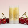 Two lip balm tubes with cherry design on a light pink background with cherries.