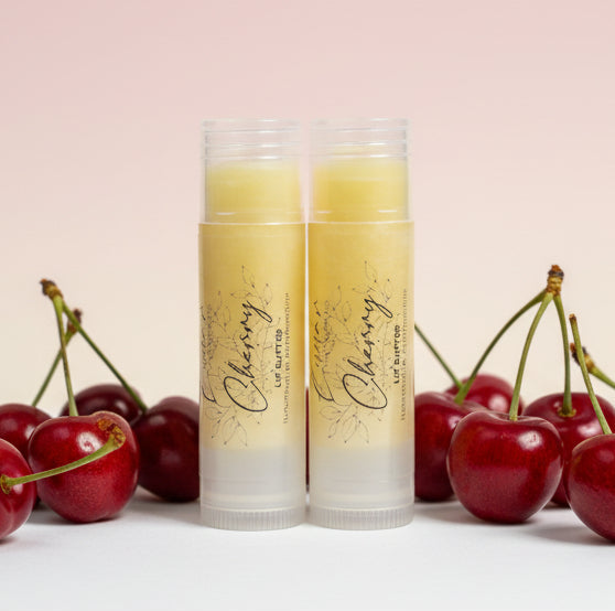 Two lip balm tubes with cherry design on a light pink background with cherries.