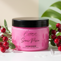 Pink sugar scrub jar with black lid surrounded by red berries and green leaves on a light background